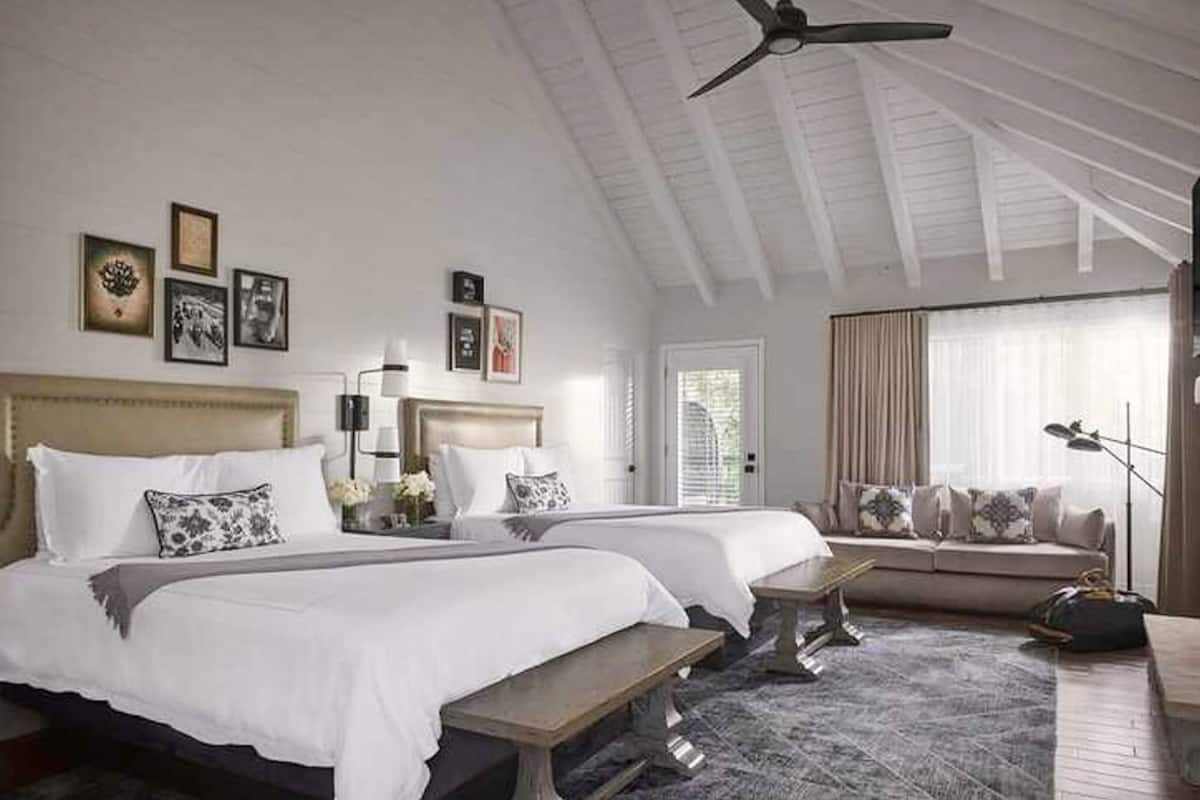 A hotel room with two beds, a bench, a sofa, and a ceiling fan.