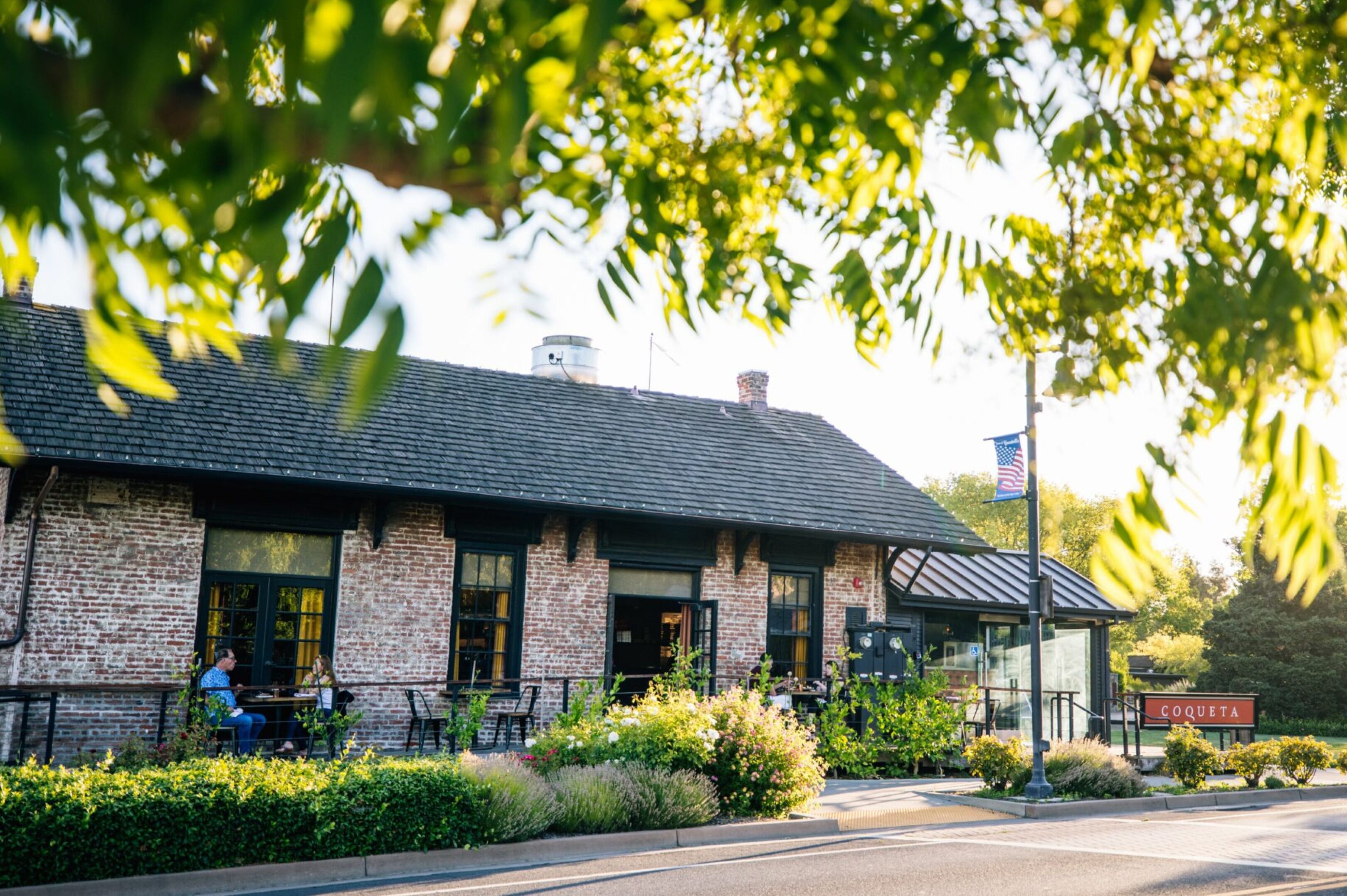 A brick building with a sign reading "COQUETTA" and outdoor seating.