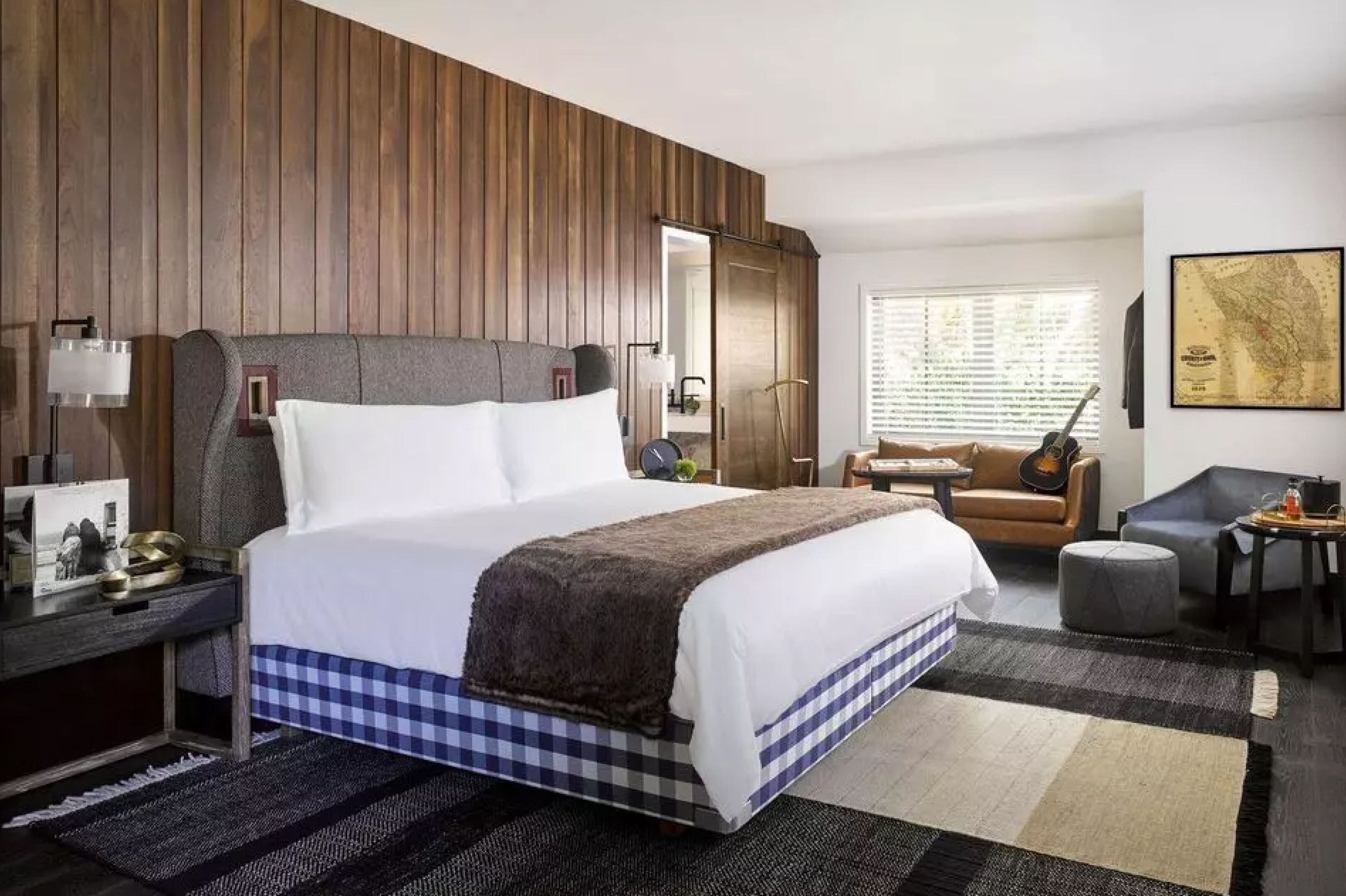 Habitación de hotel con una cama grande, un escritorio con lámpara, una silla, una guitarra y un mapa en la pared.