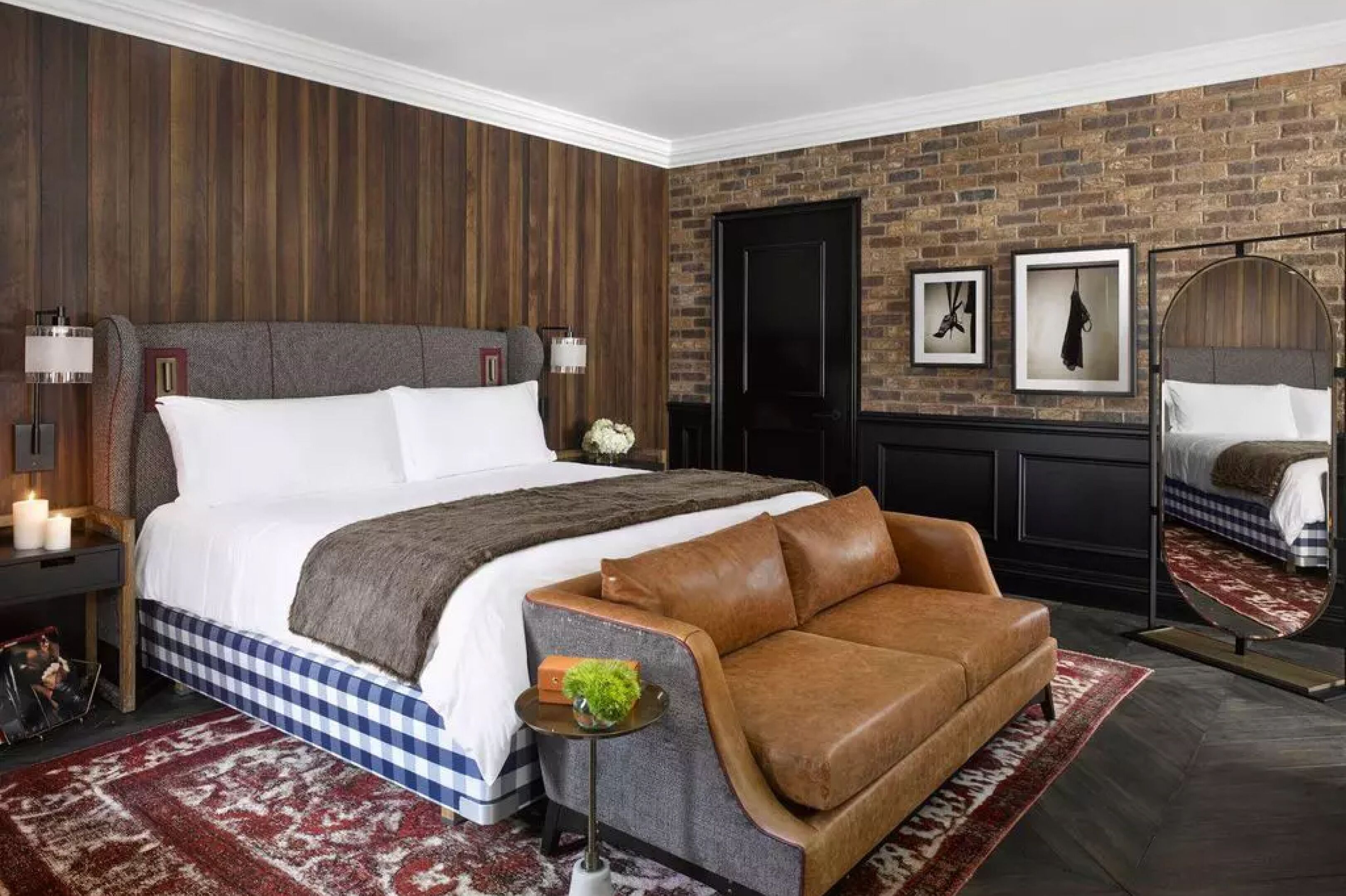 Una habitación de hotel moderna con una cama grande, un sofá de cuero, una mesita auxiliar pequeña y una pared de ladrillo.