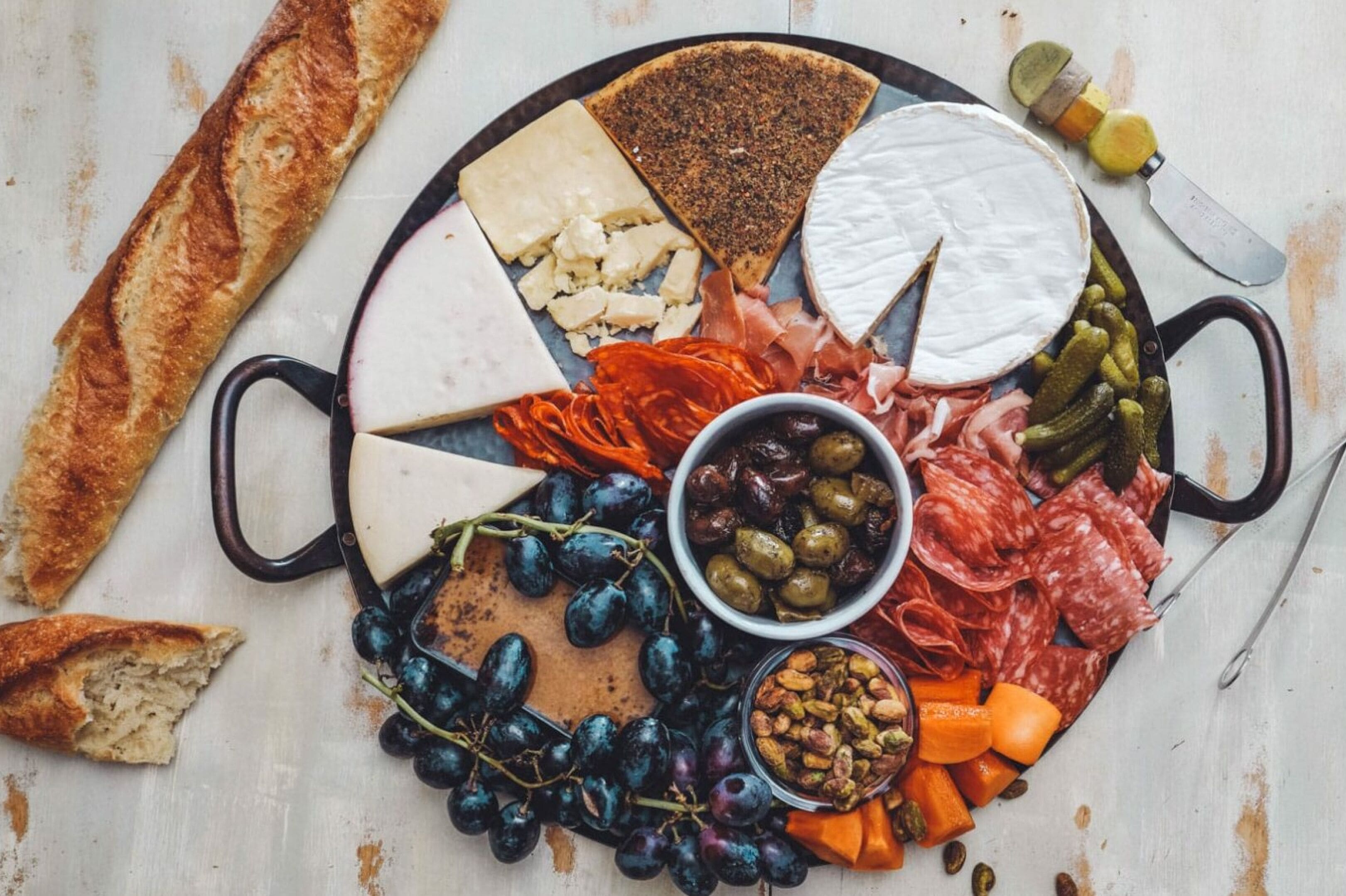 A charcuterie board with various cheeses, meats, grapes, olives, and pickles.