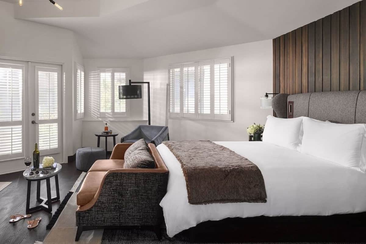 A modern bedroom with a large bed, a seating area, and a TV mounted on the wall.