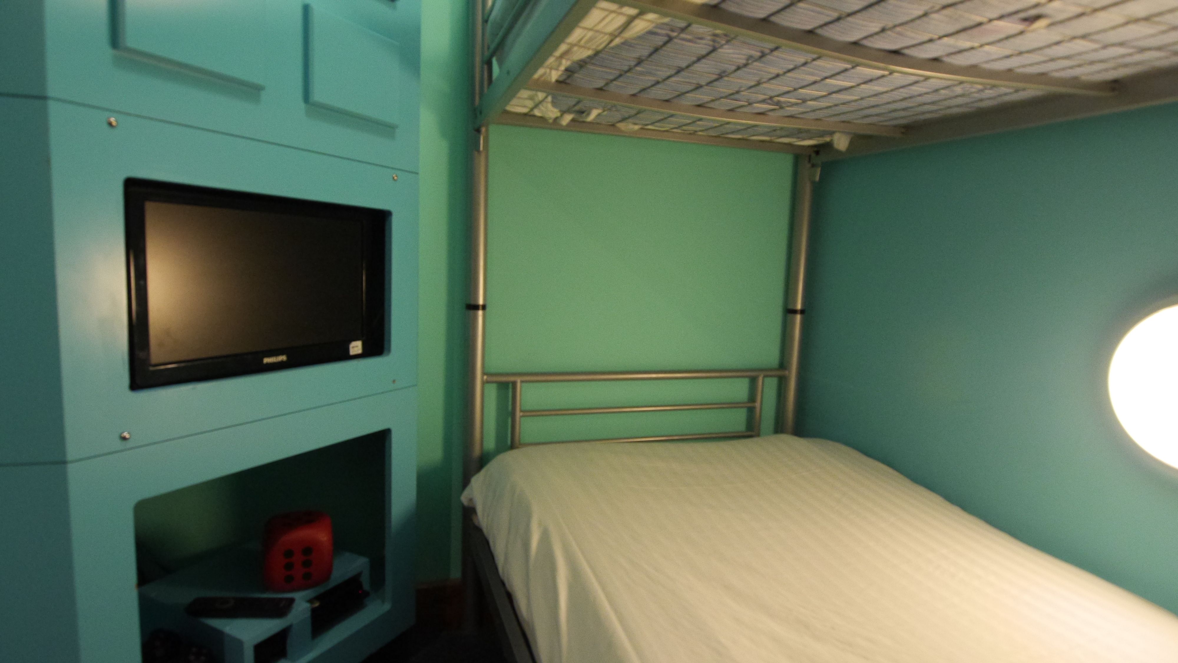 Een kleine, compacte kamer met een enkel bed, een televisie en een plank met een rood object.