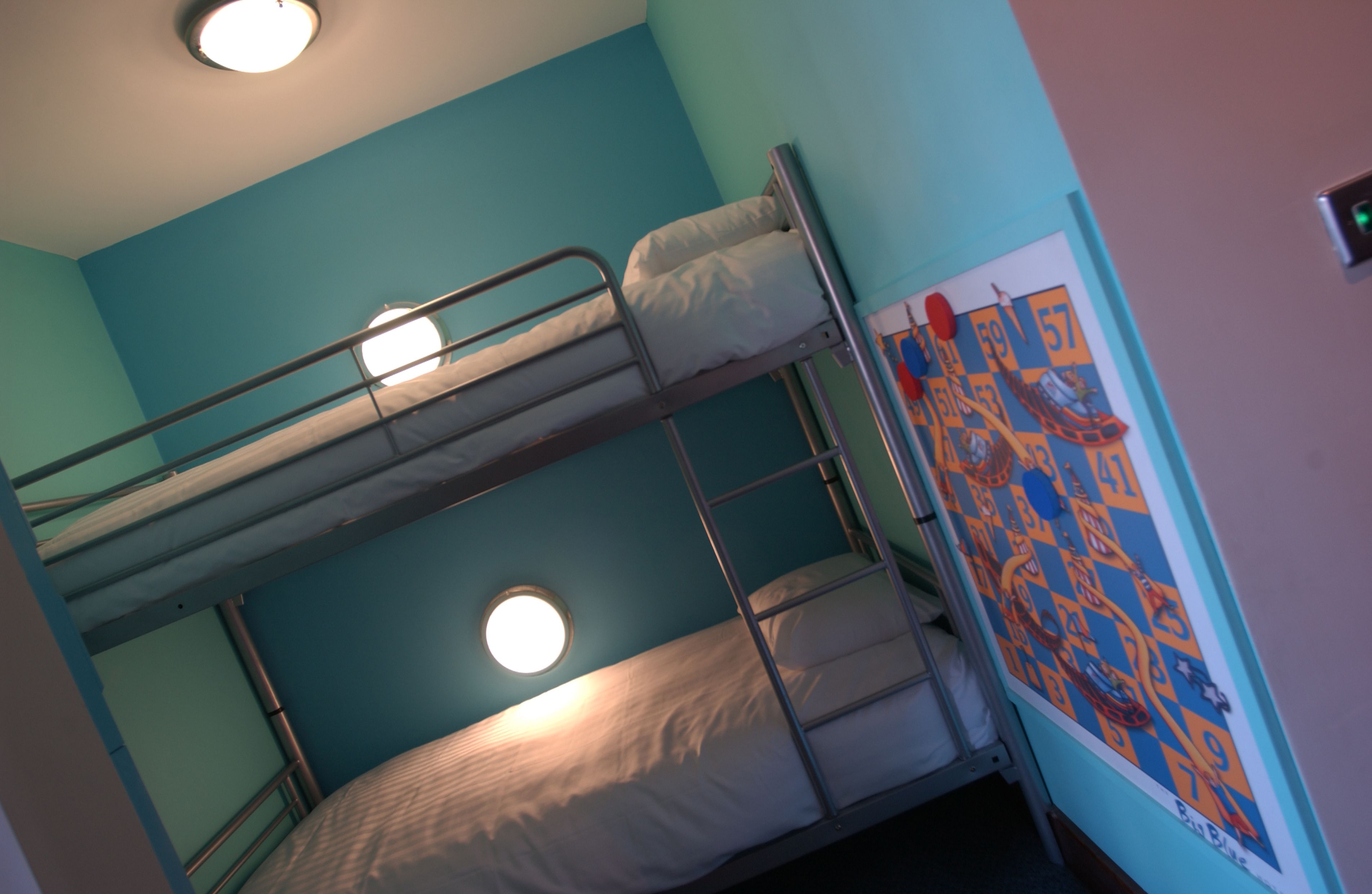 A bunk bed room with a ceiling light, a window, and a colorful wall decoration.