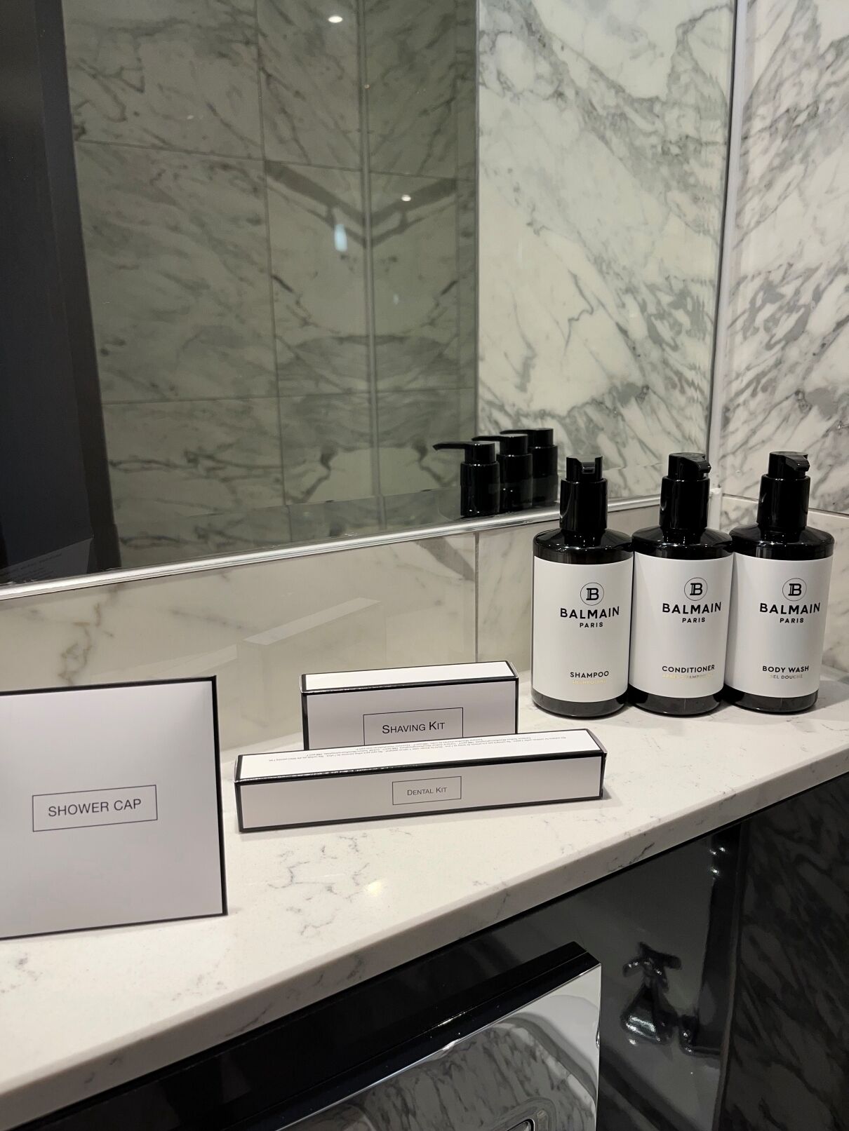 Kylpyhuoneen allaskaappi, jossa on peili, marmorinen taso sekä valikoima Balmain Paris -tuotesarjan hygieniatuotteita, kuten shampoo, hoitoaine ja suihkugeeli.