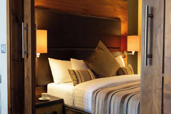 A hotel room with a large bed, two bedside lamps, a nightstand, and a cup on the nightstand. - Big Blue Hotel (Blackpool)