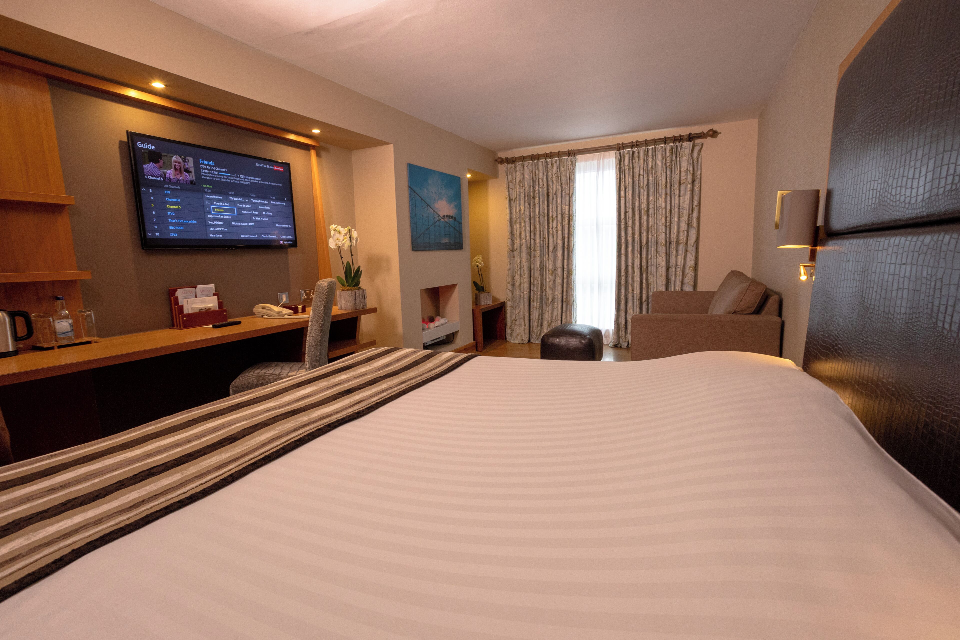 Habitación de hotel con una cama grande, un escritorio con televisor de pantalla plana, un sofá y una ventana con cortinas.
