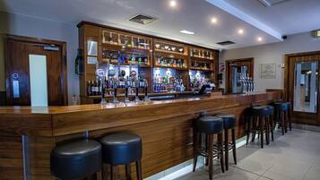 A bar area with wooden counter, multiple stools, and a variety of bottles and glasses.