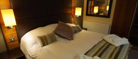 A hotel room with a large bed, two bedside lamps, a headboard, a mirror, and a towel with "Big Blue Hotel" branding.