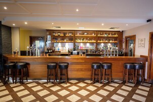Een bar met een houten toonbank, verschillende krukken en gevulde flessenrekken.