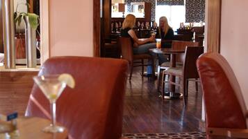 Interior de restaurante con suelo de madera, sillas de cuero y una barra al fondo.