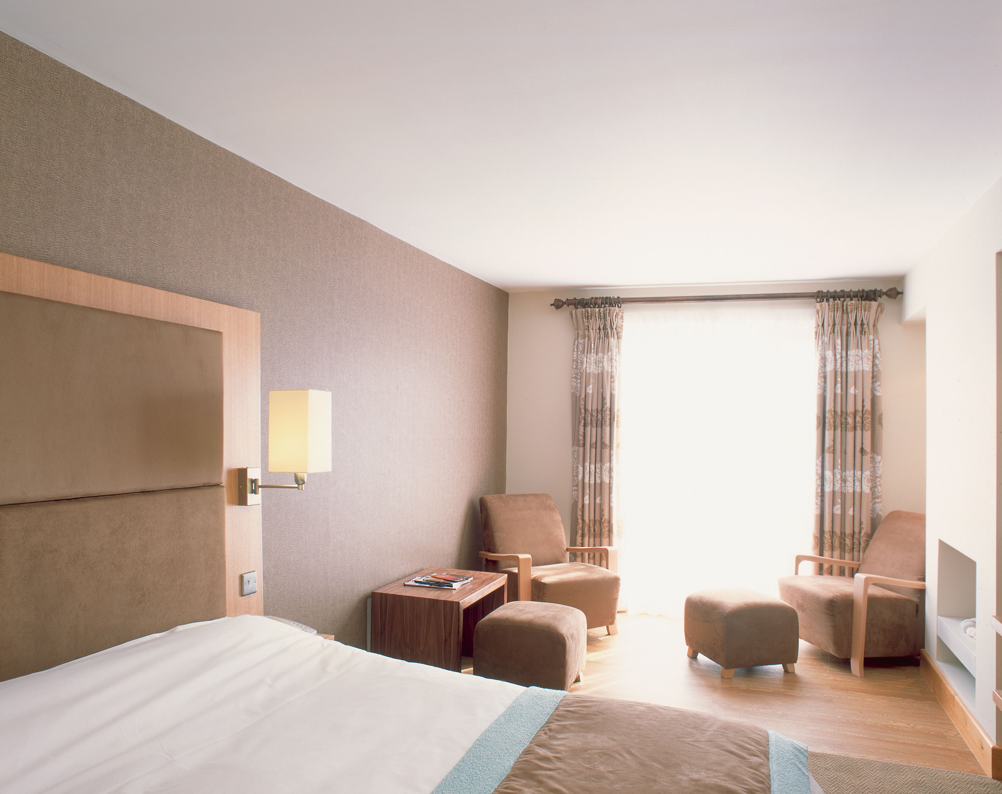 A hotel room with a large bed, two armchairs, a small table, and a window with curtains.