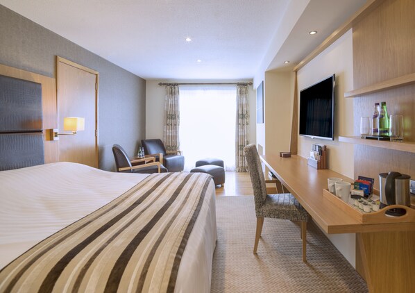 A hotel room with a large bed, a desk with a chair, a television, and a minibar.