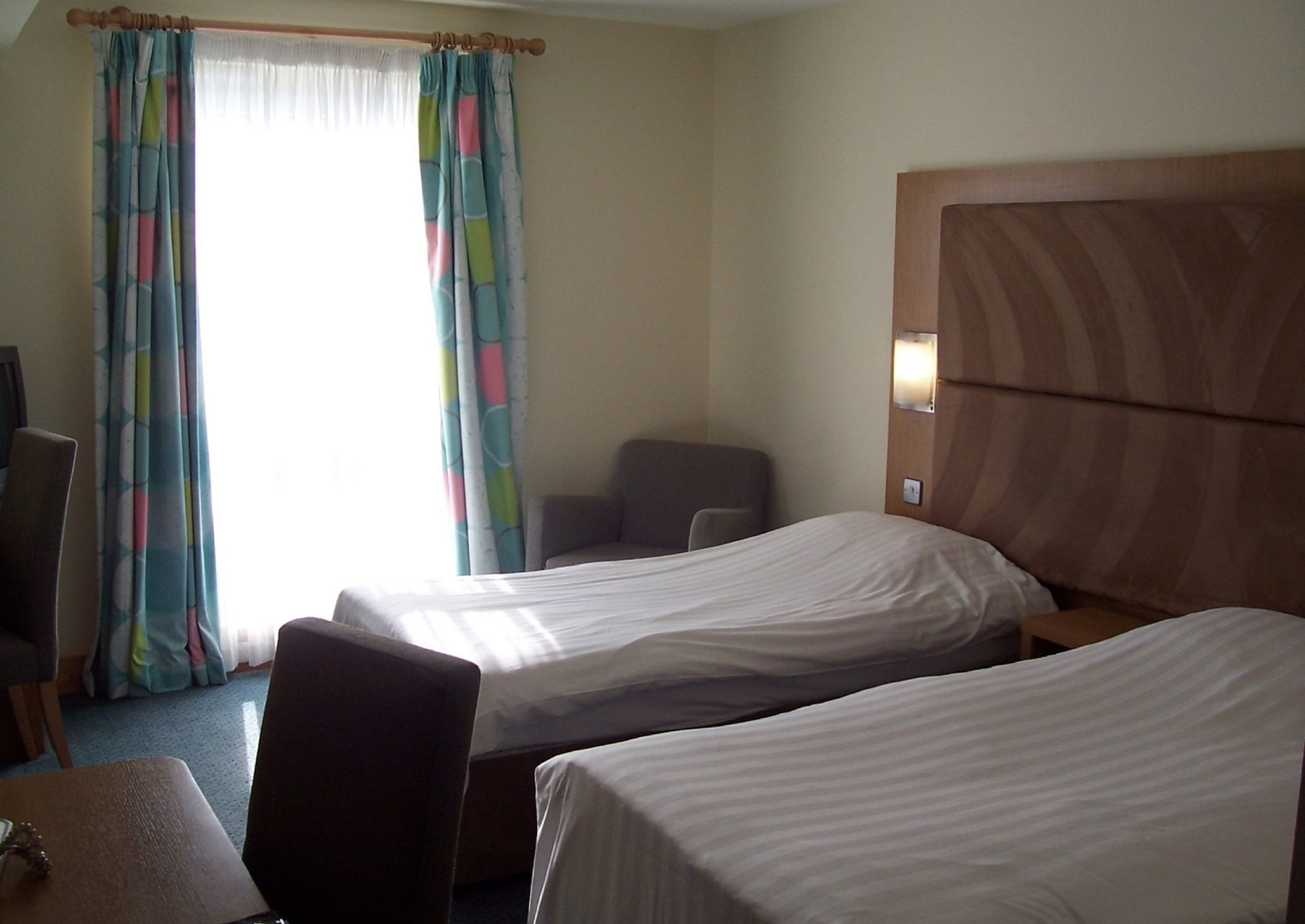 A hotel room with two single beds, a wooden headboard, a desk, and a chair.