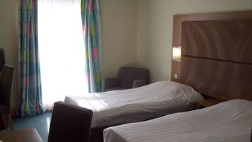 A hotel room with two single beds, a wooden headboard, a desk, and a chair.