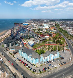 A coastal amusement park with roller coasters, a parking lot, and a seaside view. - Big Blue Hotel (Blackpool)