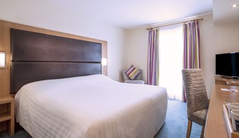 Een hotelkamer met een groot bed, een houten hoofdbord, een televisie en een bureau met een stoel.