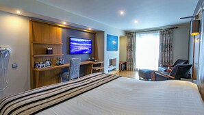 Habitación de hotel con una cama grande, un escritorio con computadora, una silla, un televisor y una ventana con cortinas.