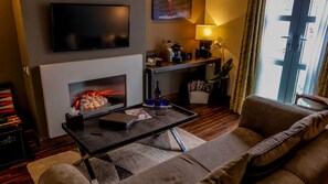 Een moderne woonkamer met een open haard, een flatscreen televisie, een bank en een salontafel met tijdschriften en een fles.
