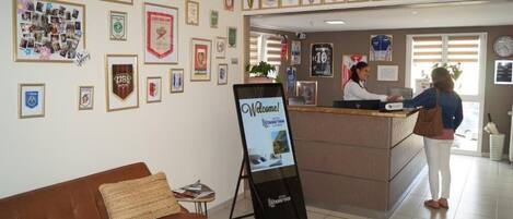 A hotel reception area with framed awards on the walls, a reception desk, and a signboard.
