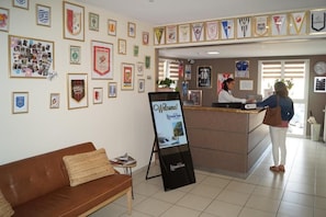 A hotel reception area with framed awards on the walls, a reception desk, and a signboard.