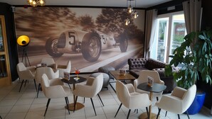 A modern lounge area with a racing car mural, comfortable seating, and a large potted plant.
