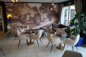 Un área de descanso moderna con un mural de un auto de carreras, asientos cómodos y una planta grande en maceta.