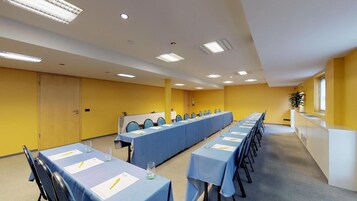 Un salón de conferencias con varias mesas, sillas y una larga mesa con mantel azul.