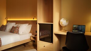 A bedroom with a bed, a desk with a globe and a laptop, and a small shelf.