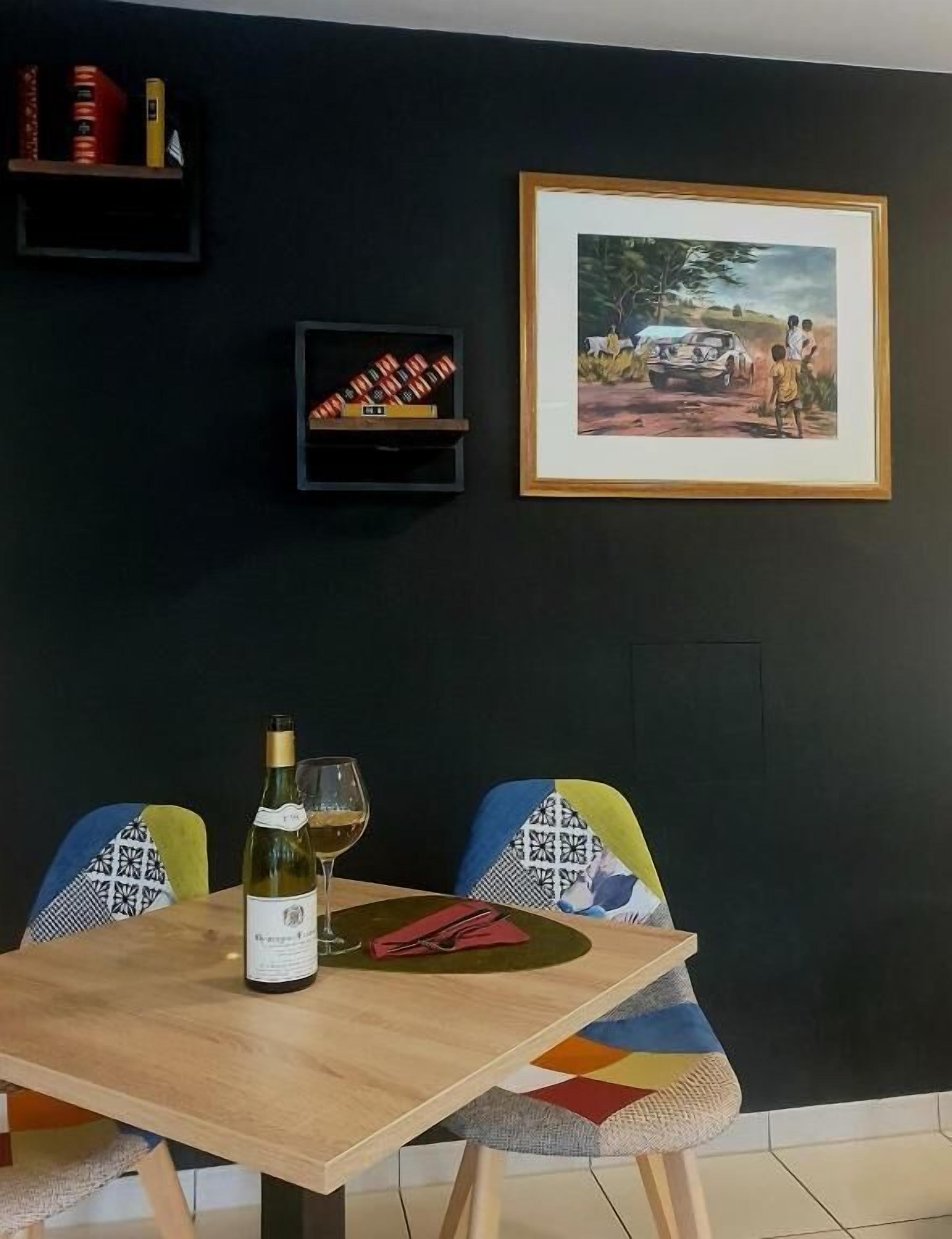 Ein Essbereich mit Tisch, Stühlen, einer Weinflasche und einem gerahmten Bild an der Wand.
