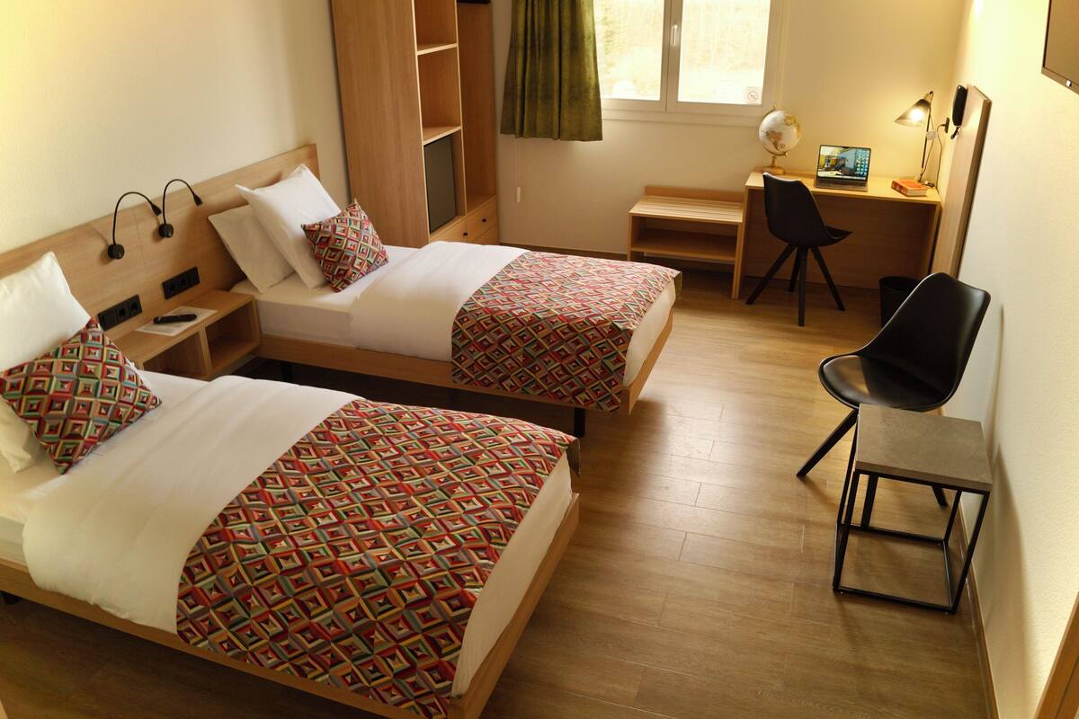 A hotel room with two beds, a desk, a chair, and a globe on the desk.