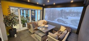 A cozy indoor seating area with wicker furniture, a coffee table, and a large window offering a view of a snowy landscape. - Hotel Stand'Inn (Mondercange)