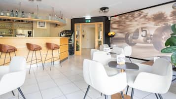 A modern bar area with stools and a counter, a seating area with tables and chairs, and a wall with a vintage racing car image.