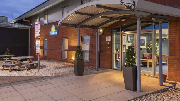 Et Days Inn hotel med overdækket indgang, udendørs siddepladser og juletræer.