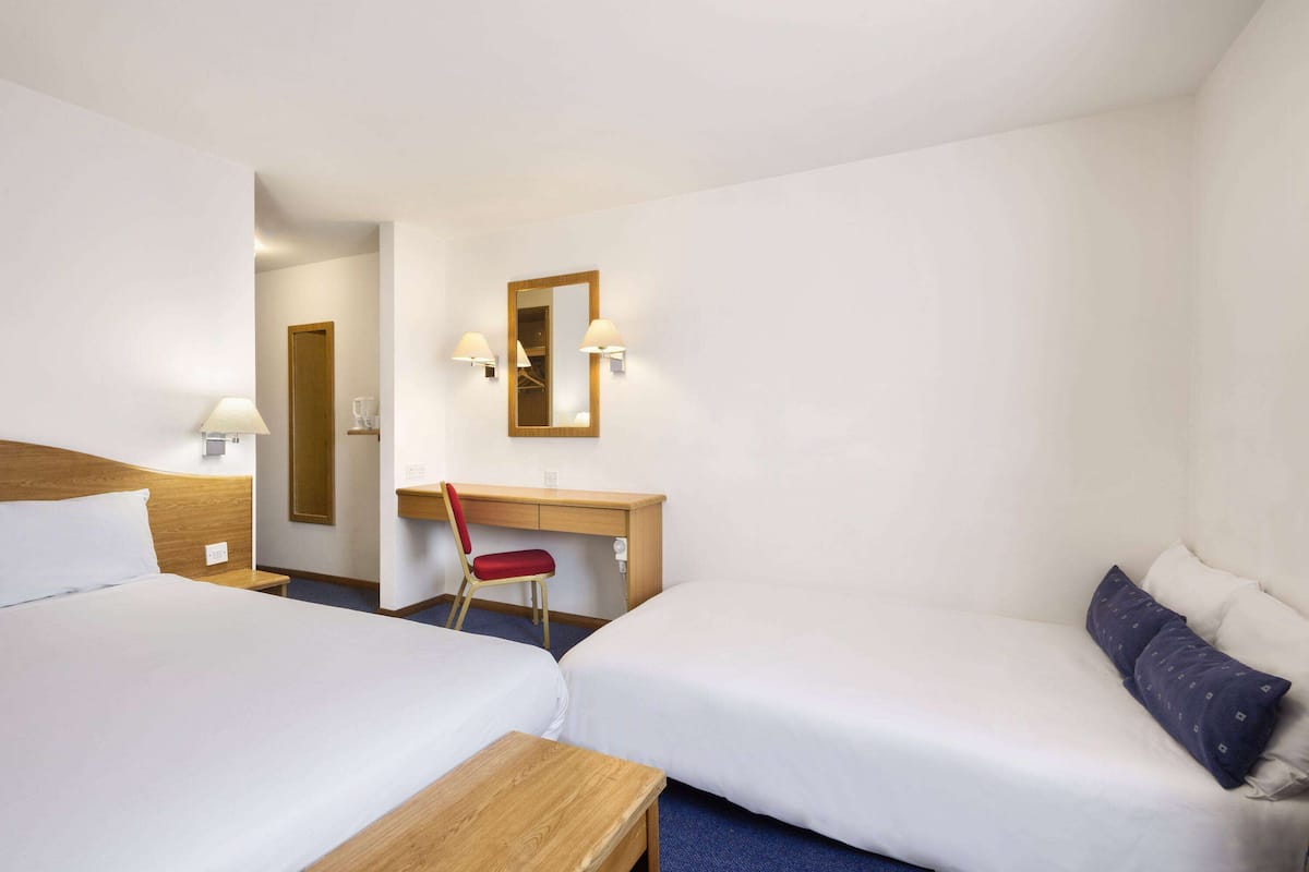 A hotel room with two beds, a desk, a chair, and a mirror.