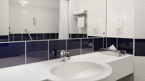Et moderne badeværelse med en hvid vask, en kromarmatur, et glasbadeværelsesafskærmning og en væg med skakmønstrede fliser.