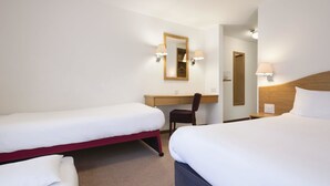 Et hotelværelse med to enkeltsenge, et skrivebord, en stol, et spejl og vægmonterede lamper.