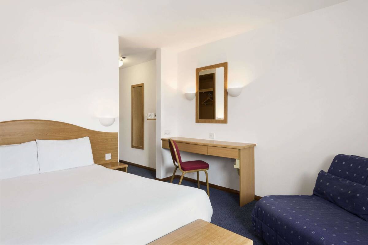 A hotel room with a bed, a desk, a chair, a sofa, and a mirror.