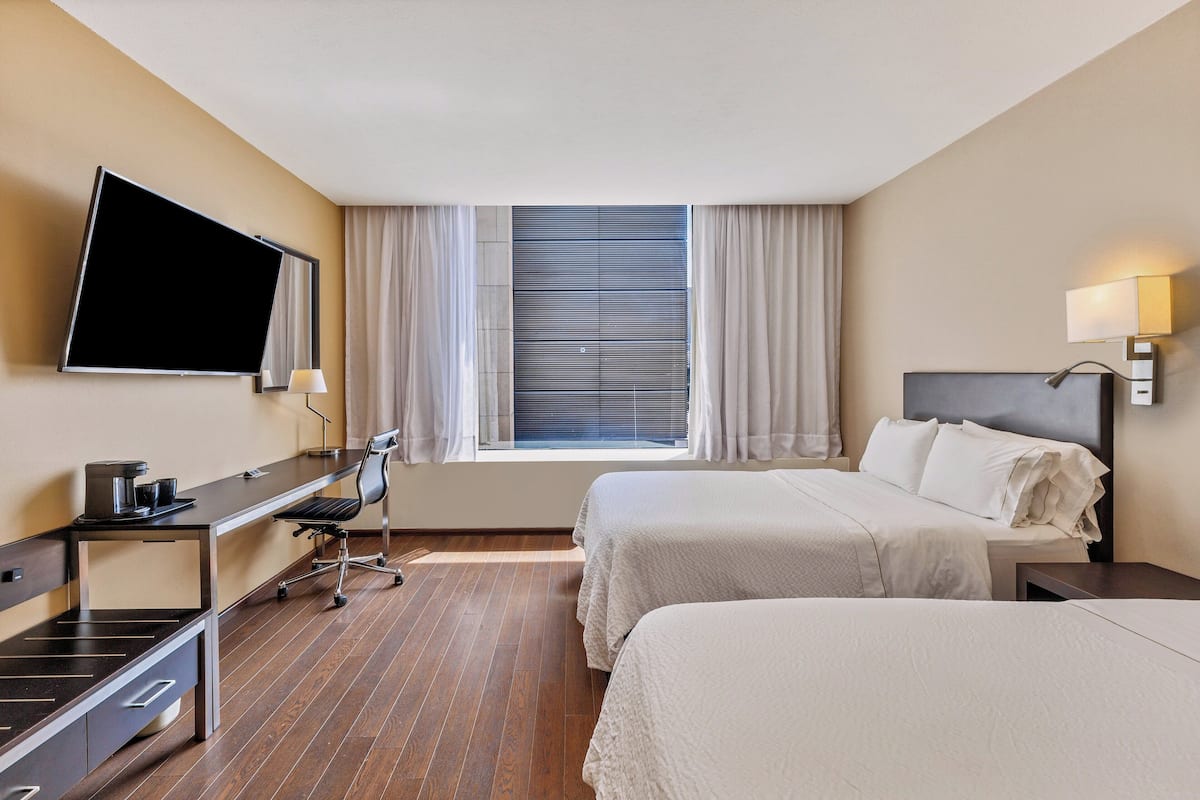 A hotel room with two beds, a desk with a chair, a TV, and a window with curtains.