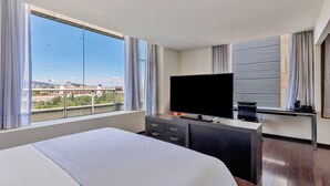 Habitación de hotel con una cama grande, televisión, escritorio y vista a la ciudad.