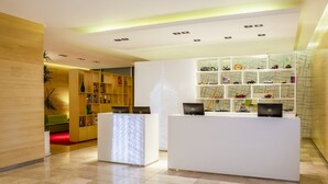 Zona de recepción con un escritorio blanco, una pantalla digital y una estantería con temática de mapas.