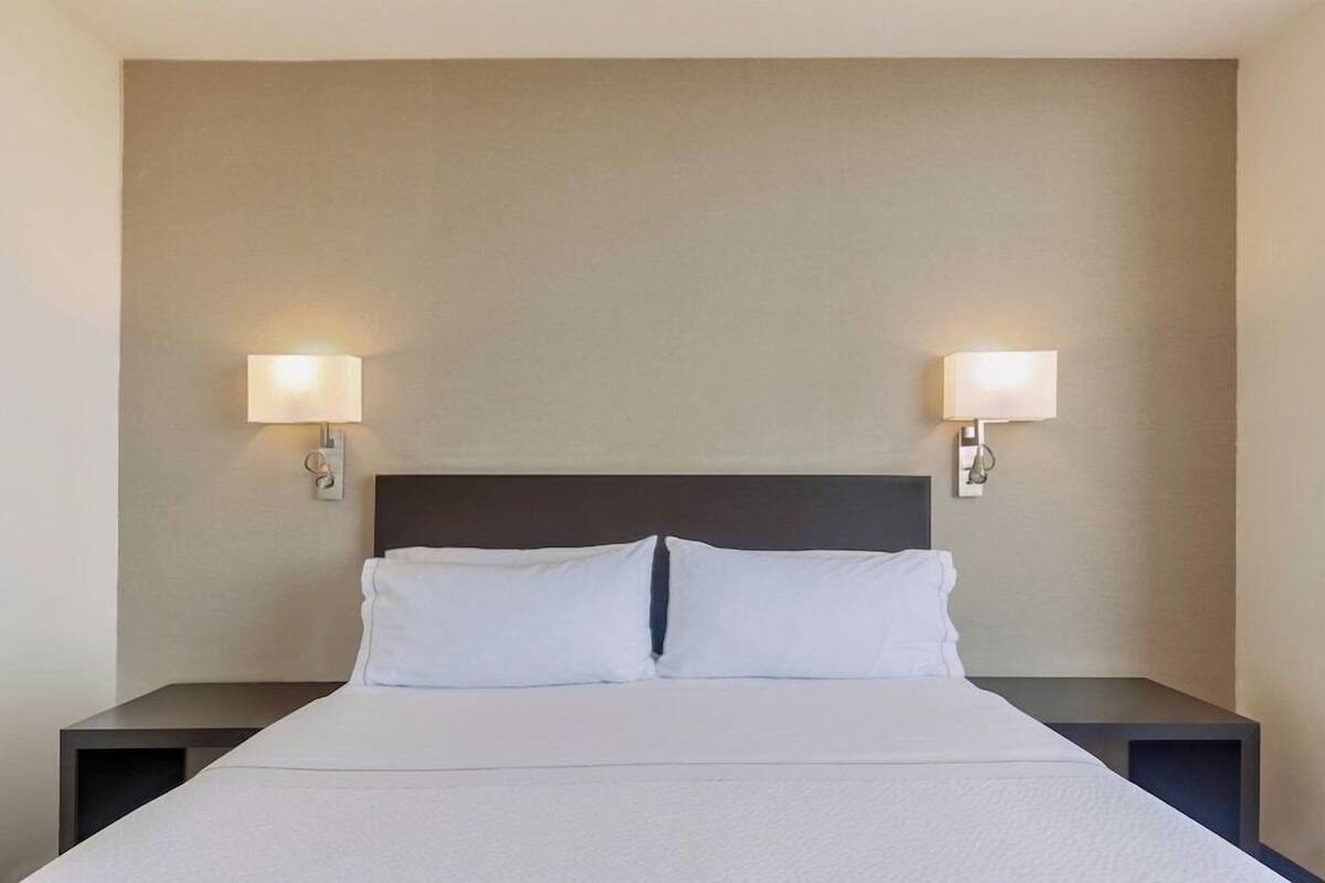 A hotel room with a bed, two bedside tables, and wall-mounted lamps.