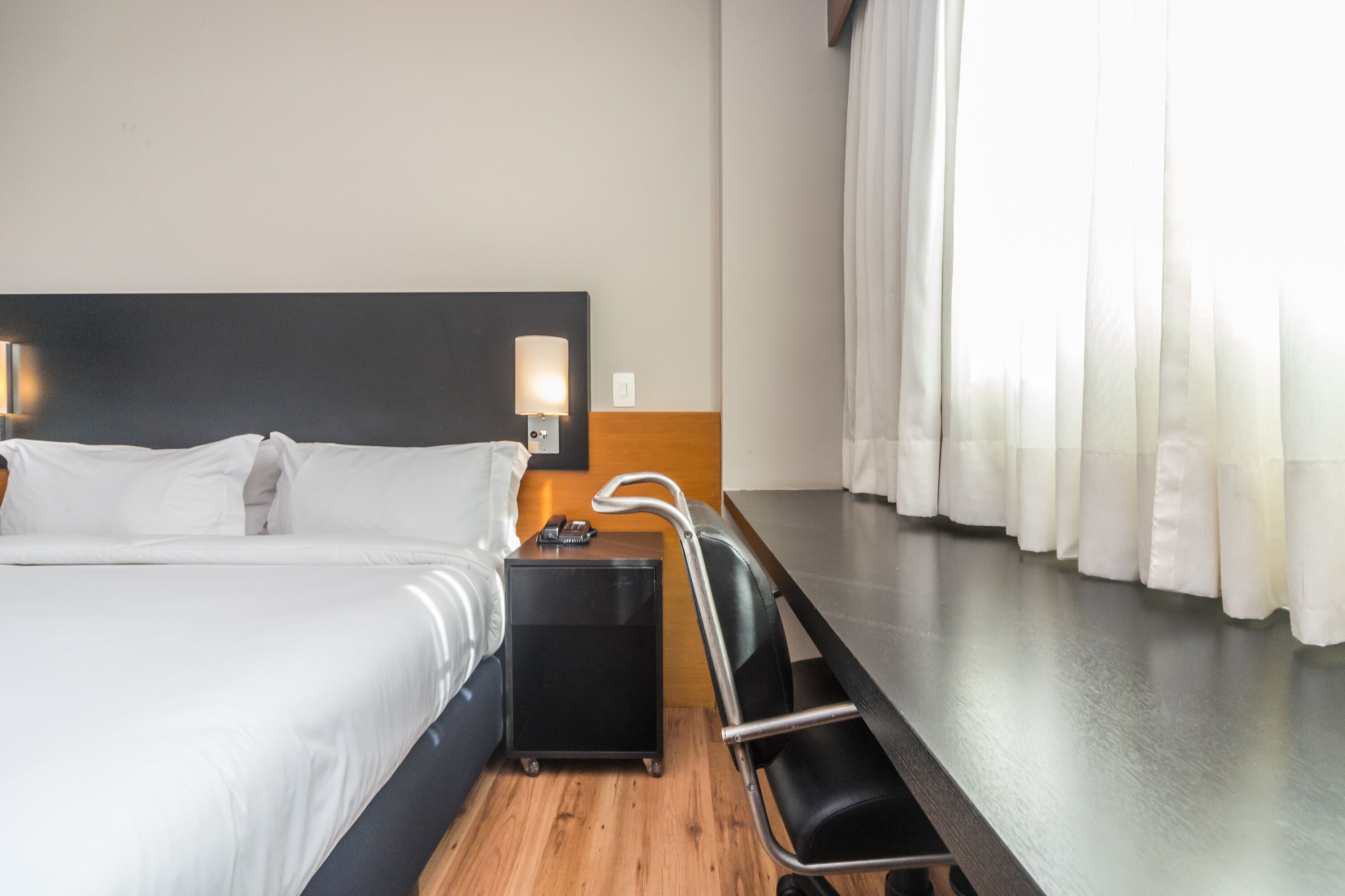 Een hotelkamer met een bed, nachtkastje, lamp en een stoel.
