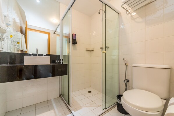 A modern bathroom with a glass-enclosed shower, a white toilet, and a black countertop with a sink. - Paraíso Suítes by Charlie (São Paulo)