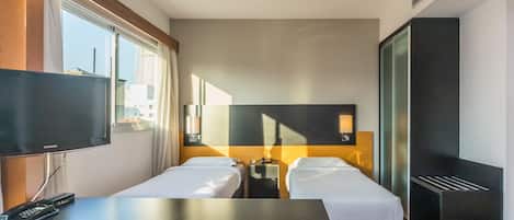 A hotel room with two single beds, a flat-screen TV, a desk, and a wardrobe.