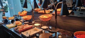A buffet area with various food items displayed in baskets and trays, illuminated by overhead lamps. - Paraíso Suítes by Charlie (São Paulo)