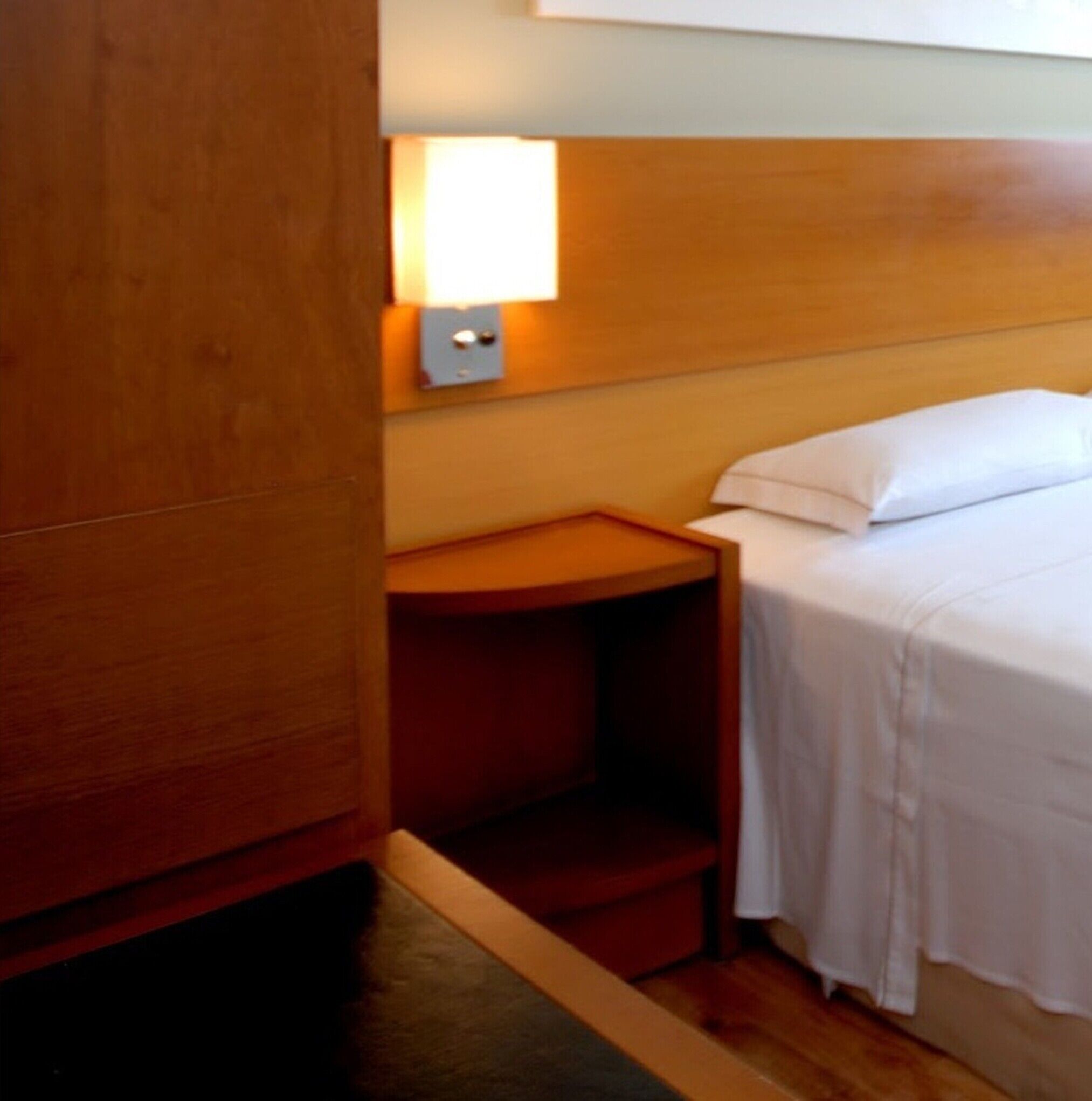 A hotel room with a bed, a nightstand, a wall-mounted light, and a wooden wardrobe.