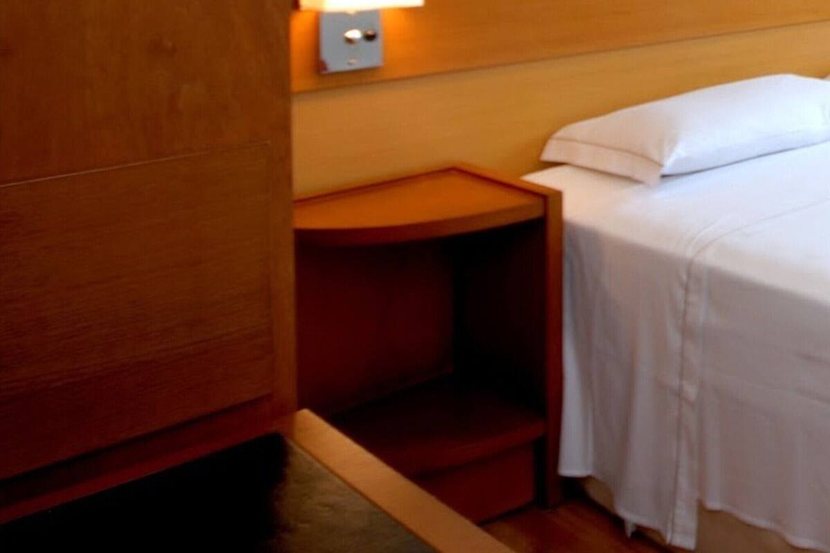 A hotel room with a bed, a nightstand, a wall-mounted light, and a wooden wardrobe.