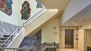 Un interior moderno con una escalera de mármol, un ascensor y una pared decorada con mosaicos.