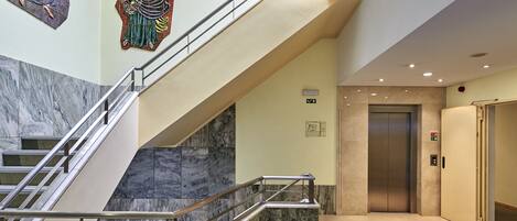 A modern interior with a marble staircase, an elevator, and a wall with mosaic artwork.